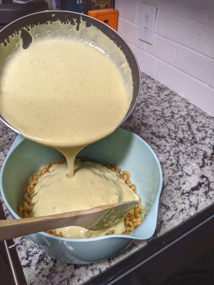 Pouring the garlicky&nbsp;vegan cheese sauce over cooked elbow macaroni.